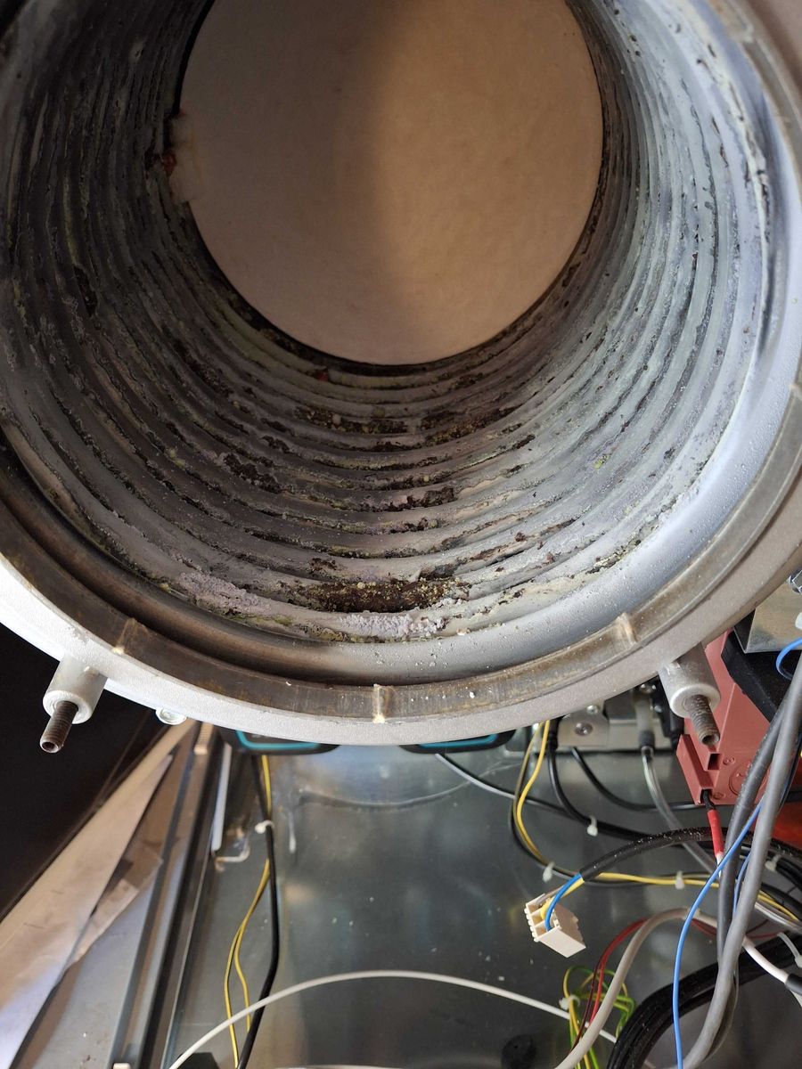 Interno dello scambiatore di un modulo a condensazione visto dal lato fumi, con depositi chiari e macchie scure sulle spire