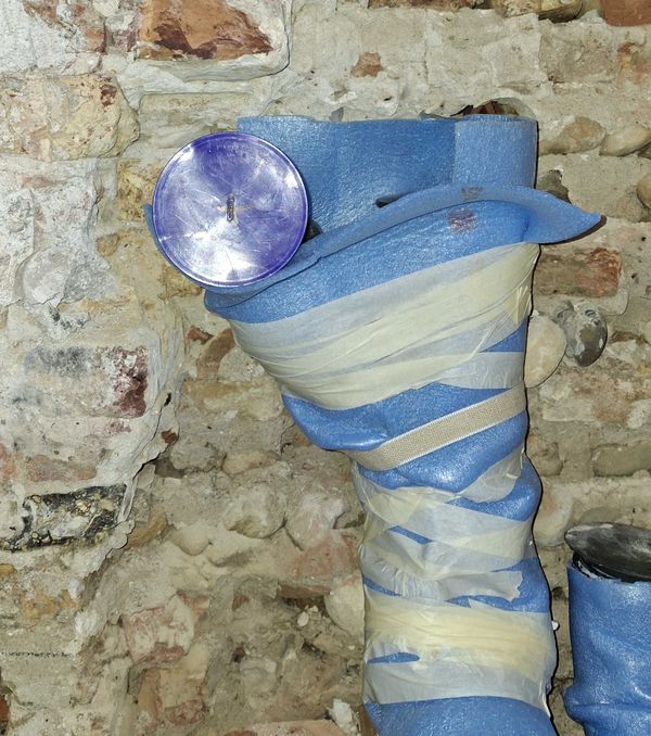 Braga di scarico con tappo di ispezione viola, protetta da guaina e nastro contro il muro in mattoni