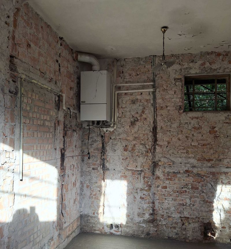 Stanza dell’edificio in restauro con muri in mattoni a vista, vecchia caldaia murale e tubazioni esistenti